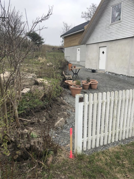 Öppen yta vid bakre huset med grusstig, planteringskrukor och ett vitt staket.