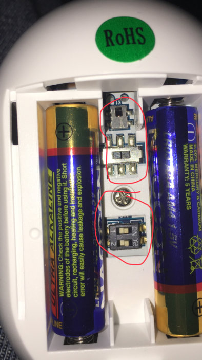 Inre delen av ett Kerui G19 larm visar batterifack och kretskort med två AA-batterier och märkning RoHS.