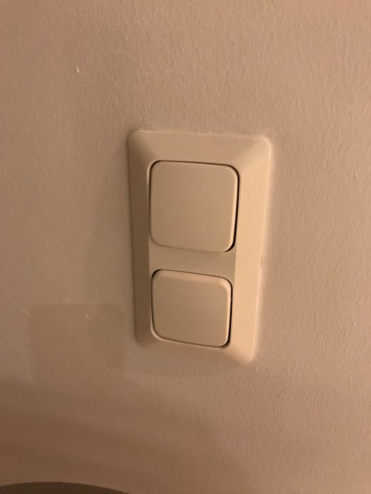 Väggmonterad vit strömbrytare med två vippor mot beige vägg.