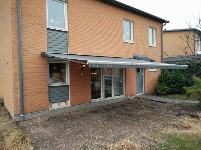 Utskjuten elektrisk markis med sensorer på ett tegelhus, ovanför terrassdörrar och fönster.