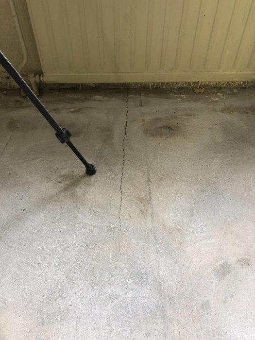 Sliten betongplatta med synliga sprickor nära väggen och en stor spricka som korsar golvet.