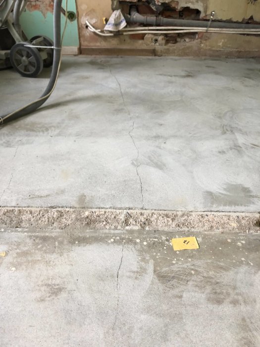 Slipad betongplatta med synliga sprickor nära vägg och över ytan, spår av limrester och gamla trösklar synliga.