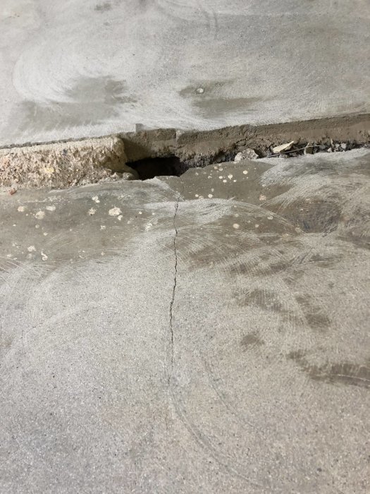 Betongplatta i kök med tydlig spricka och hål där en gammal tröskel eller vägg varit.