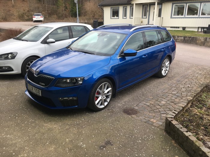 Blå Skoda Octavia parkerad på en grusparkering med hus i bakgrunden.