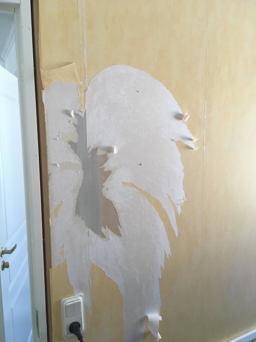 Vägg under renovering med delvis borttagen tapet och synliga hyvelmärken på skarven.