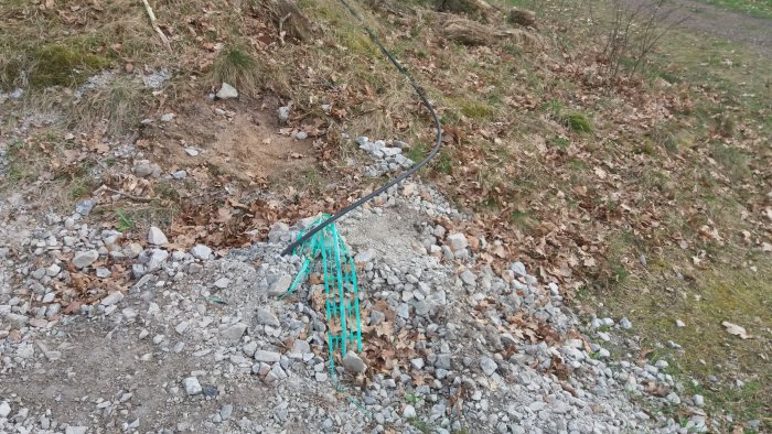 Utmärkt elledning med en grön skyddsnät längs en nyligen grävd tomt, omgiven av grus och löv.