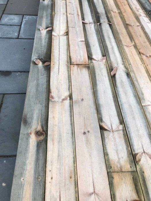 Närbild på gråsvart missfärgad kärnfurutrall med synliga träknutar och skruvhål på en terrass.