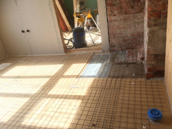 Pågående flytspacklingsarbete i ett badrum med nät på golvet och omgivande väggar i olika material.