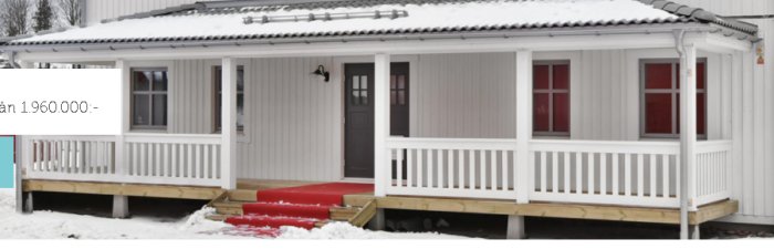 Vit enplansvilla med veranda och räcke under vinter, snö runt huset, prisangivelse synlig.