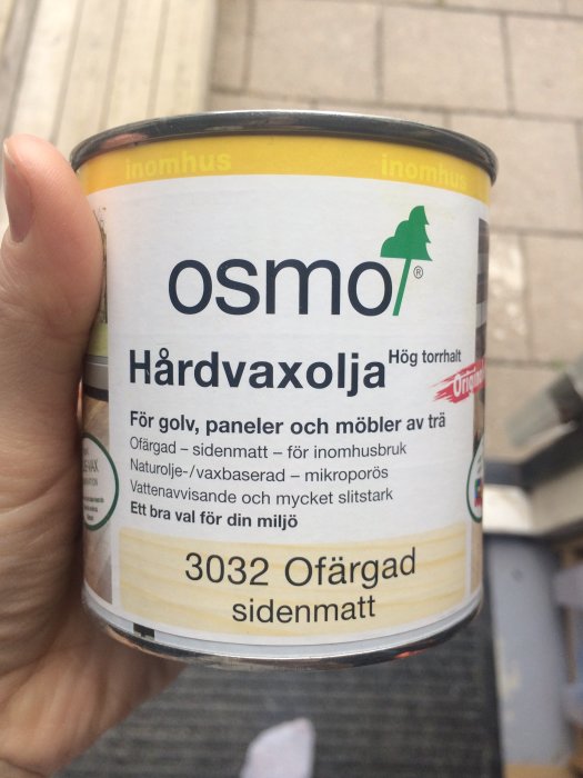 Hand håller en burk Osmo Hårdvaxolja för inomhusbruk med texten "3032 Ofärgad sidenmatt" synlig.