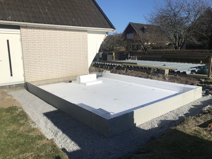 Nyinstallerad grund av plattor för byggprojekt bredvid ett befintligt hus.