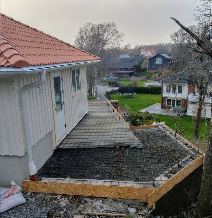 Förberedelser för gjutning av terrass med armeringsnät och träformar vid hus.