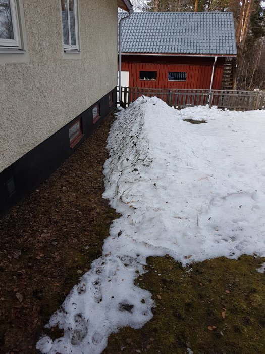 Husvägg med smältande snö bredvid, trolig orsak till läckage vid bergvärmerören i källaren.