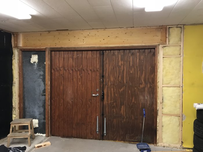 Garage med äldre slagportar och delvis exponerad isolering inför renovering.