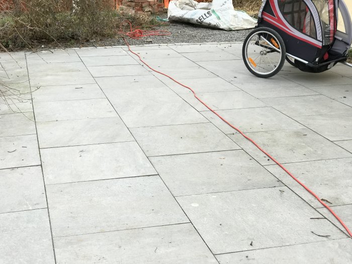 Nyinstallerade betongplattor på en utomhusgångväg med en röd förlängningssladd och del av en cykelkärra i kanten.