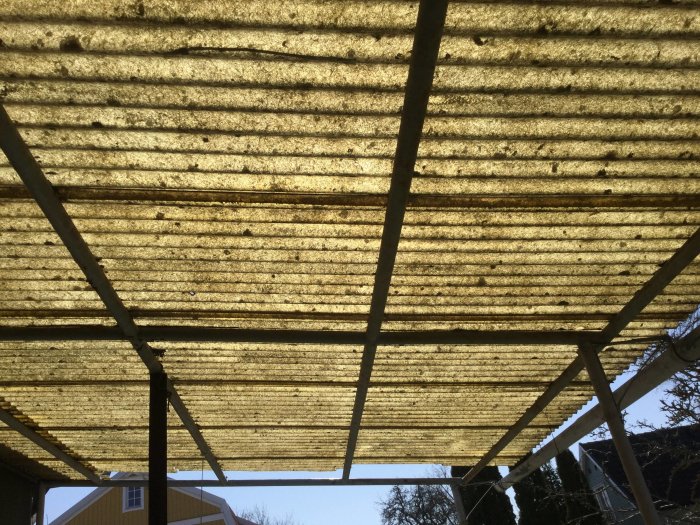 Ett gammalt smutsigt PVC-tak sett underifrån med synlig trästomme och bakgrund av klar himmel.