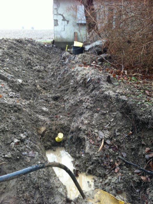 Elkabel nerskarvad i grävd grop med 50mm rör som leder till ett fasadmätarskåp vid byggnad.