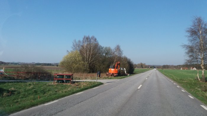 Grävmaskin vid vägkanten antyder arbete på underjordiskt ledningsnät mot lantlig bakgrund.