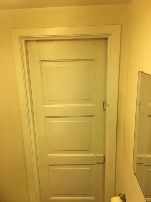 En stängd vit dörr i en gulvägg, som är i behov av renovering eller en ny färg.