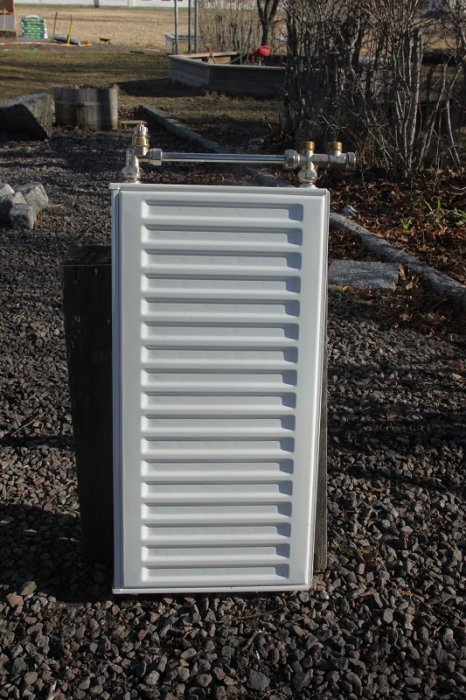 Vit Purmo-panelradiator 300x600mm med väggfästen, utomhus på grus.