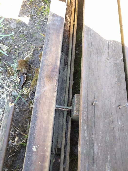 Träbrädor på en altan med en borttagen ytterbräda visar ett glapp med spik och en underliggande improviserad stödstruktur.