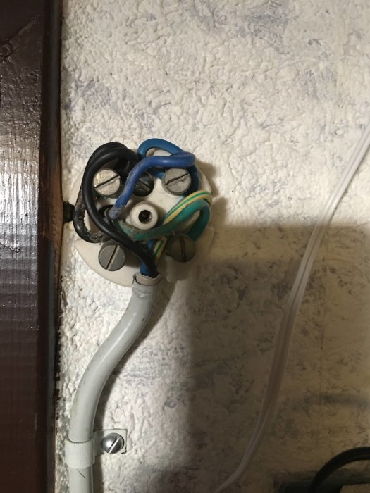Elektrisk kulledosa öppnad på vägg med trassel av kablar inklusive blå, svart och gulgrön tråd.