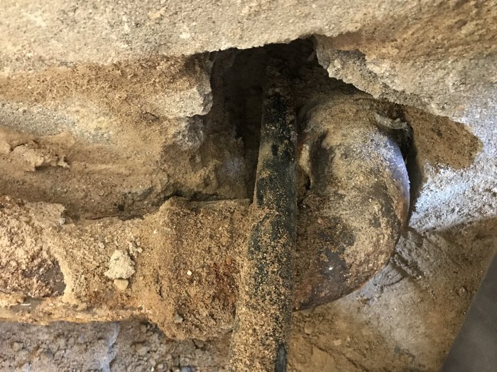Gjutjärnsrör genom betongvägg, synlig grus och jord från renoveringsprojekt.