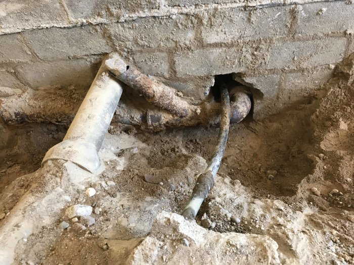 Delvis frilagda gamla avloppsrör i gjutjärn som kommer ut ur en betongvägg i en pågående renovering.