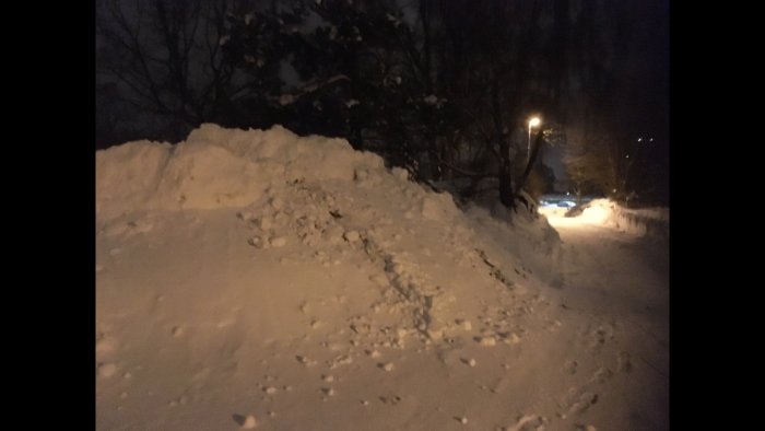 En stor snöhög på en fastighet vid en gata på natten.