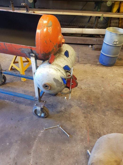 Röklåda med hästskogångjärn under konstruktion i en verkstad, gängstång och verktyg på golvet.