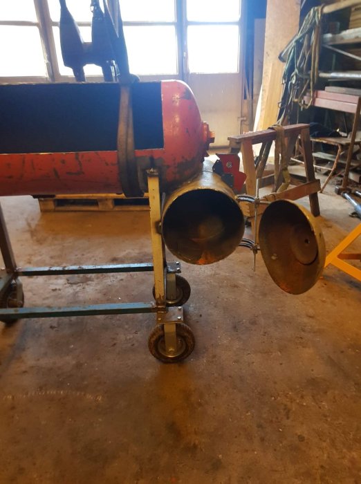 Renoverad röd och svart gammal vedpanna på hjul i ett garage.