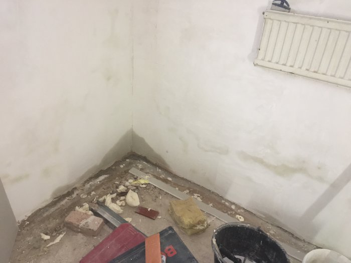 Källarhörn med fuktskador på väggen, spackel och renoveringsmaterial på golvet.