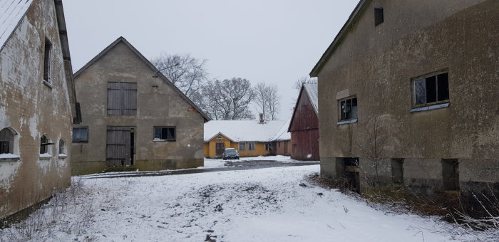 Vinterbild av övergivna byggnader på en Skånelänga med stall, täckt av snö.