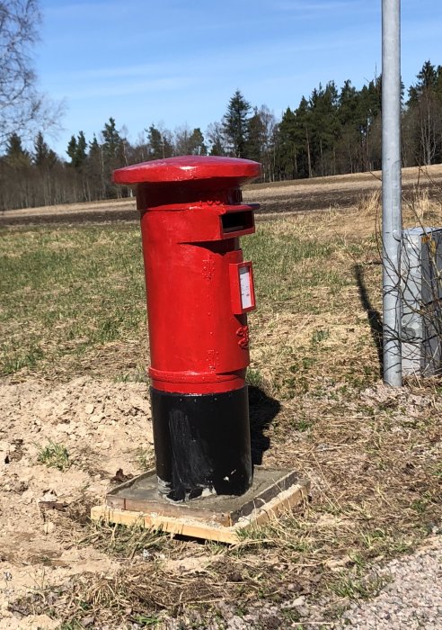 Röd brevlåda på stolpe installerad utomhus med natur i bakgrunden.