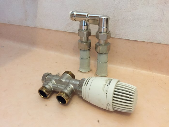 Radiatortermostat och förbigångsrör demonterade och placerade på en ljus yta under renoveringsarbete.