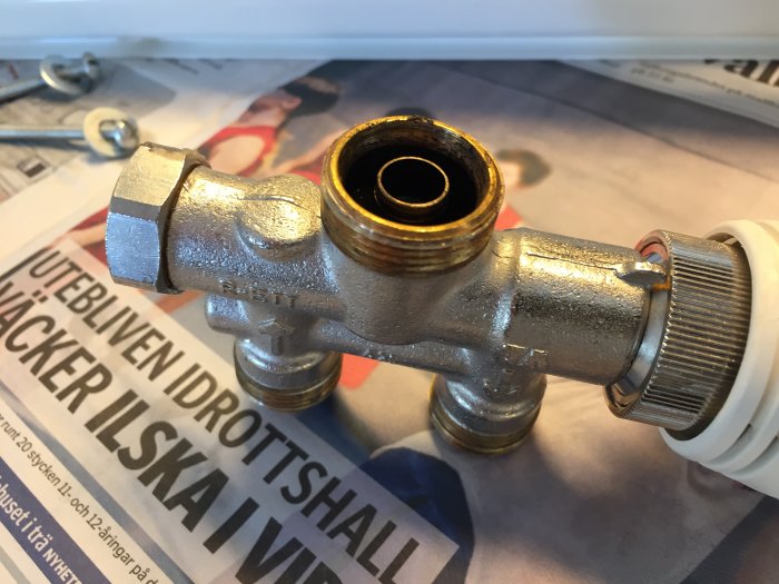 Förbigångsrör i metall med öppna anslutningar, ligger på tidning, förberedelse för VVS-installation.