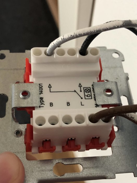 En närbild av en elektrisk korskoppling med en vit och svart sladd ansluten, mot en metallram.