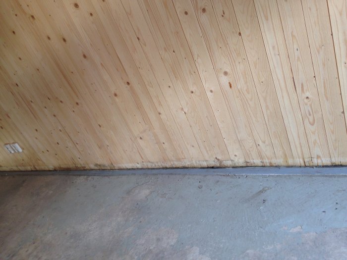 Trävägg möter betonggolv i ett ofärdigt byggprojekt, detalj av skarv.