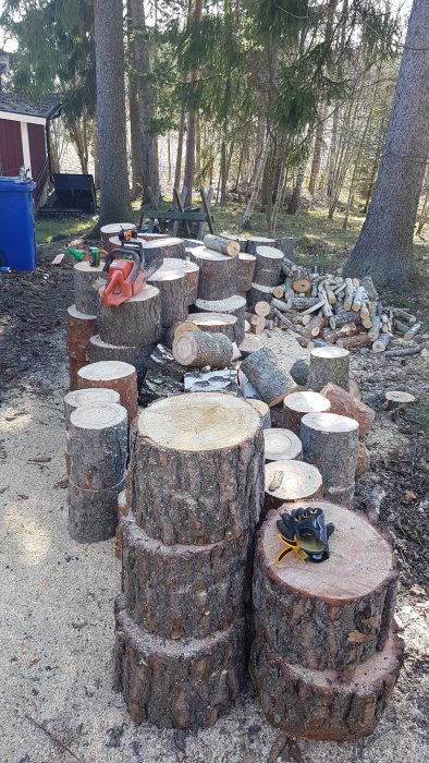 Stora vedklabbar staplade utomhus med en motorsåg och ett par handskar placerade ovanpå.