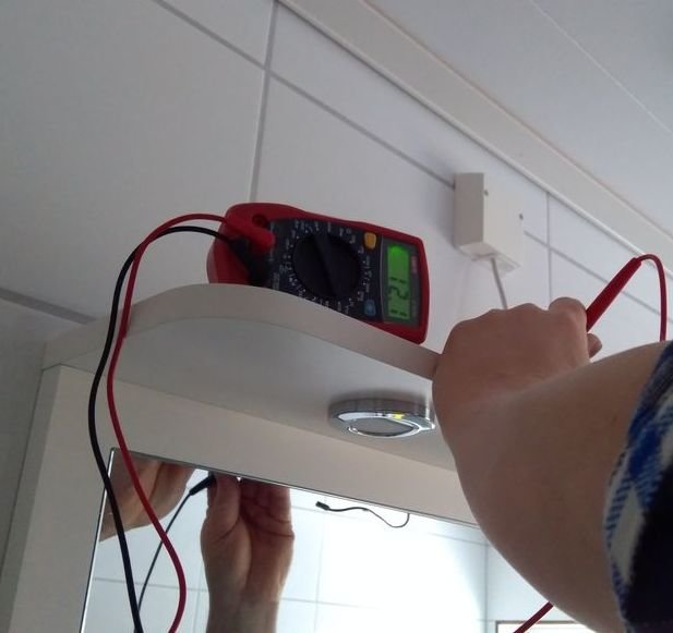 Person som mäter spänning på inbyggda spotlights i badrumsspegel med multimeter.