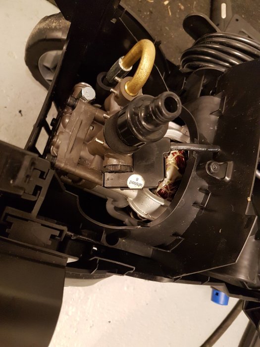 Närbild på en svart cylinder och en microswitch inuti en demonterad maskin.