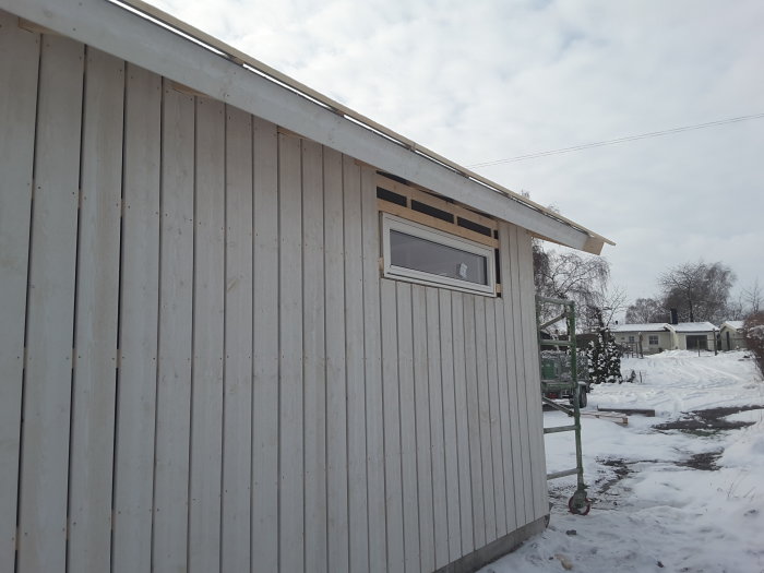 Stående träpanel på norrsidan av ett hus med fönster och snöig omgivning.