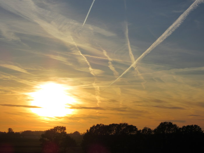 Solnedgång med korsande flygplanskontrails mot en dramatisk himmel.