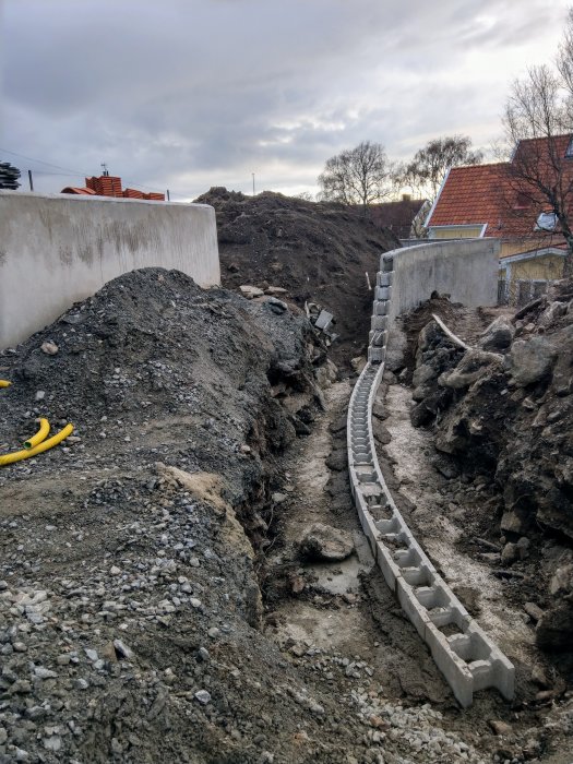 Ett pågående byggprojekt med en delvis uppbyggd mur och en nyligen gjuten terrassgrund bland grushögar.