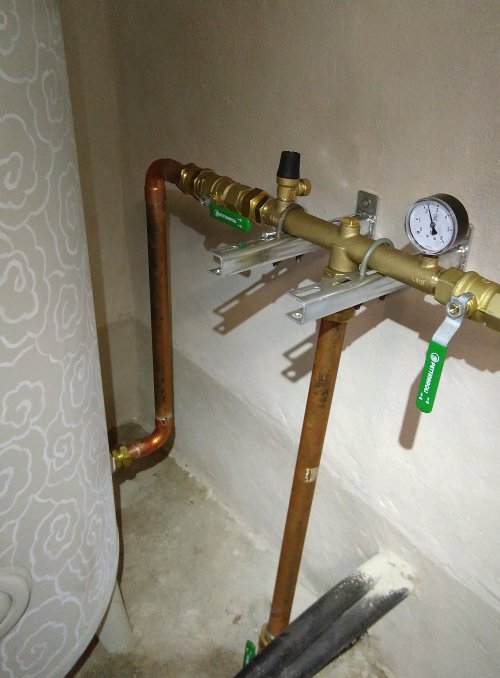 Kopparledningar med mätinstrument och reglerventiler fastsatta vid en vägg, nyinstallerade i ett hem.