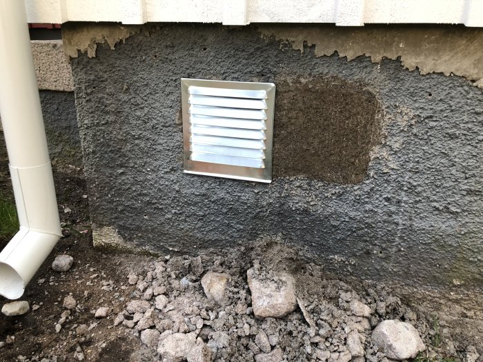 Nylagat cementbruk på husgrund med ventilation och avloppsrör, sten och grus i förgrunden.