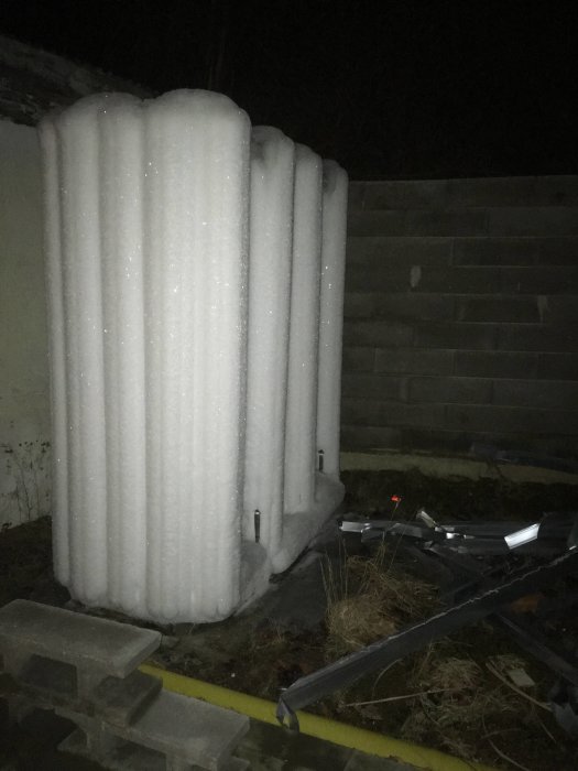 Värmepumps utedel täckt av tjocka lager is i ett bostadsområde under nattetid.