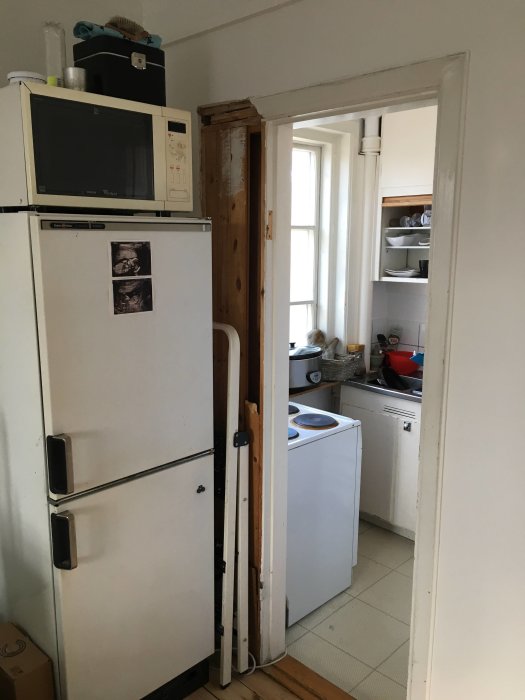 Ett litet kök med en öppen dörr, träplankor bredvid dörröppningen är delvis demonterade för breddning.
