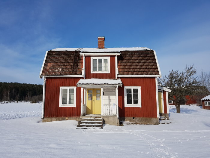 Rött traditionellt svenskt 1,5-planshus med vita knutar och snötäckt mark.