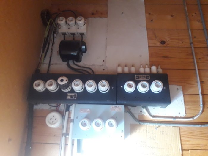 Gammal elcentral med säkringar och kablar på en trävägg, utan synlig jordfelsbrytare.